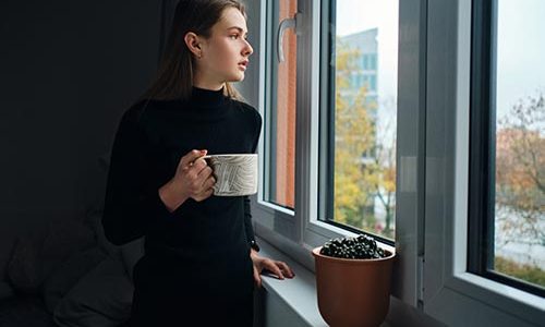 side-view-attractive-girl-holding-mug-while-thoughtfully-looking-out-window-home