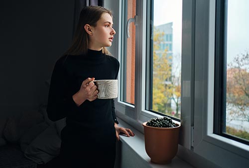 side-view-attractive-girl-holding-mug-while-thoughtfully-looking-out-window-home